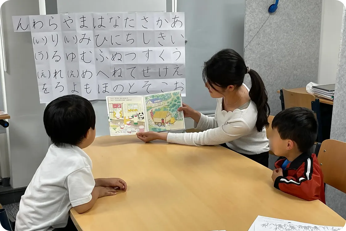 日本語の本を読み聴かせる先生と聴いている生徒 | ことば遊びクラス | Sakura 国語のワークショップ